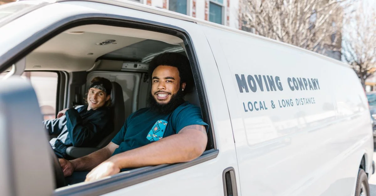 Deux déménageurs souriants dans leur camion de déménagement garé par une journée ensoleillée.