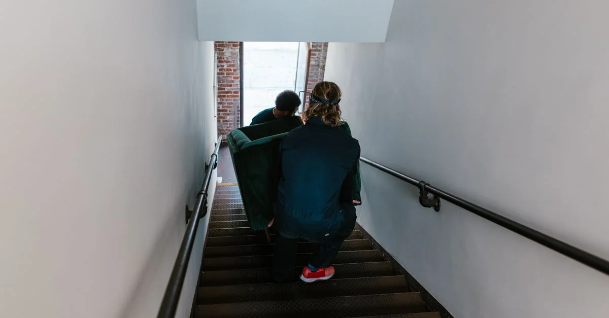Deux hommes déplacent soigneusement un canapé dans un escalier en intérieur.