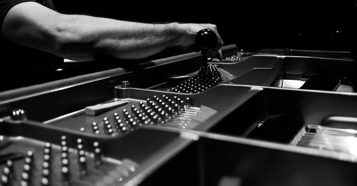Image en noir et blanc d'un accordeur de piano ajustant les cordes à l'intérieur d'un piano à queue, mettant en avant la précision.