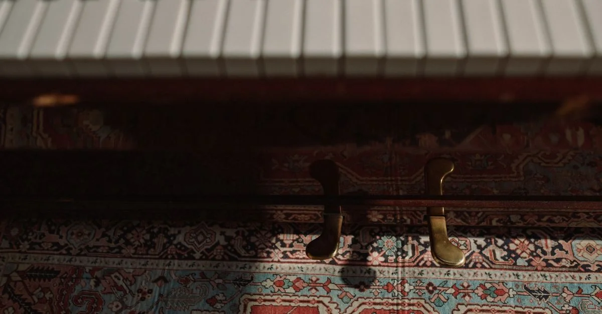Gros plan artistique des touches et pédales de piano sur un tapis à motifs vibrant dans une faible lumière.