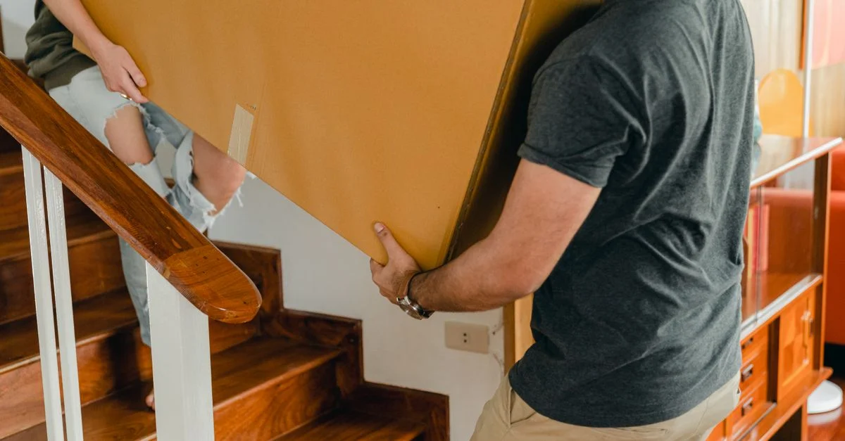 Un couple portant une grande boîte en carton dans les escaliers de leur nouvelle maison.