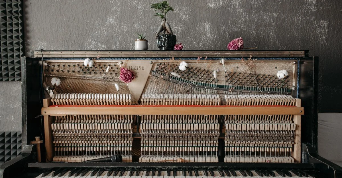 Un piano droit vintage avec des cordes exposées, orné de fleurs et d'un bonsaï, dans un cadre de studio acoustique.